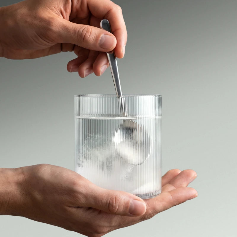 Immagine di alcune mani che sciolgono la creatina in un bicchiere d'acqua.