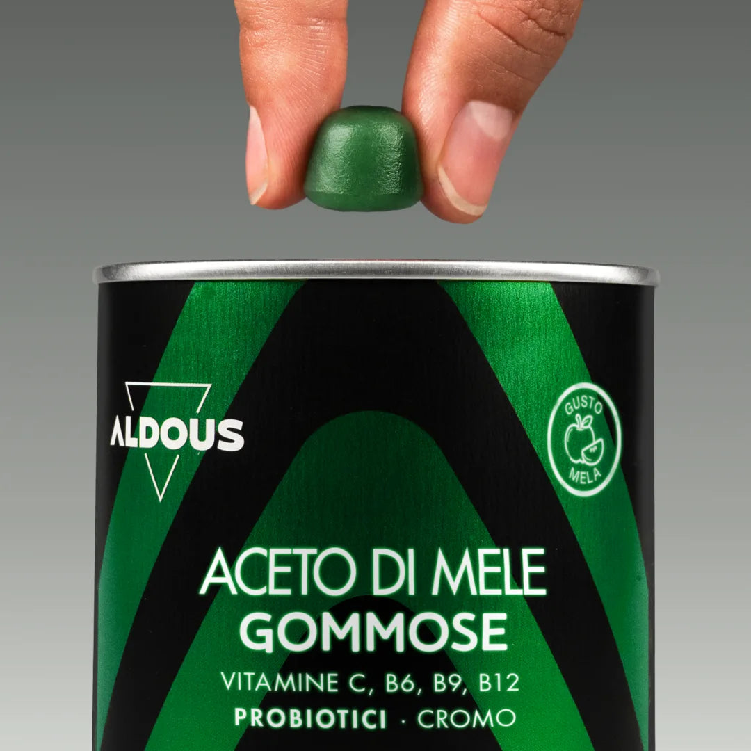 Mano che tiene una gommosa verde all’aceto di mele sopra la confezione aperta...